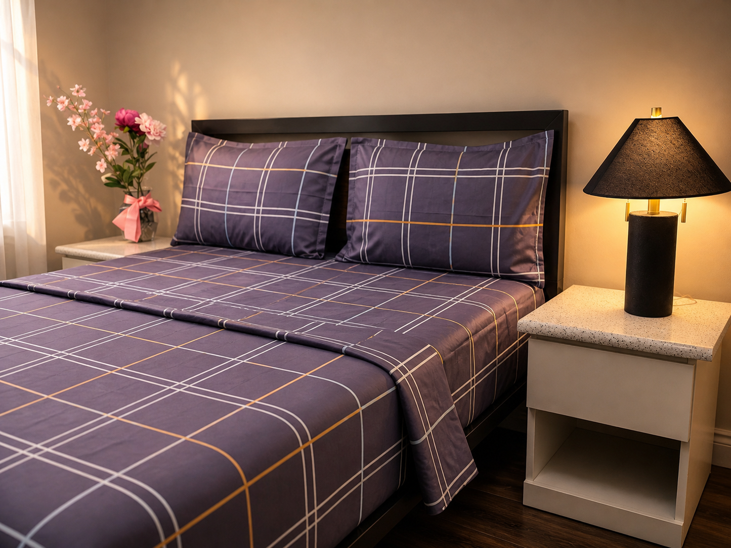 Bed with purple plaid bedding in a bedroom setting with nightstands and a lamp.