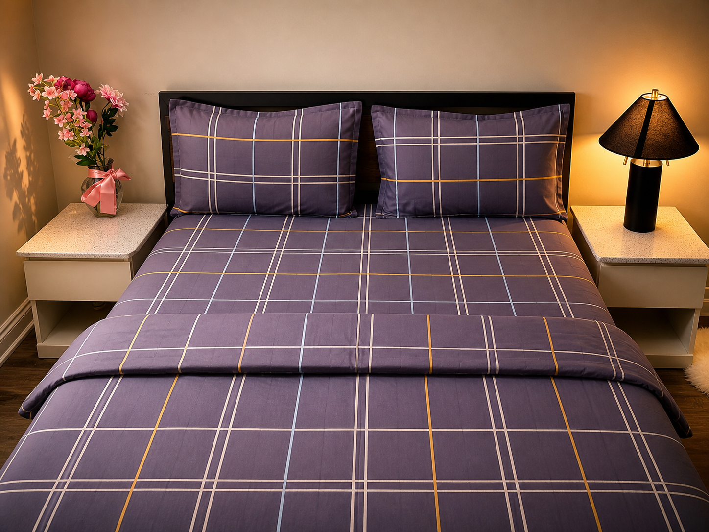 Bed with purple plaid bedding in a bedroom setting with nightstands and a lamp.