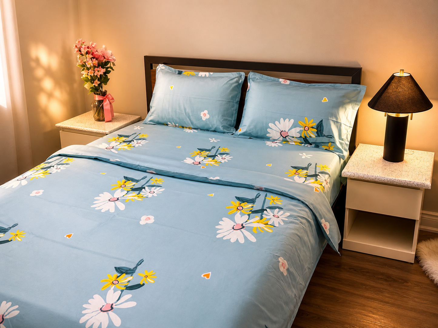 Bed with floral bedding in a bedroom setting with a lamp and flowers on a nightstand.