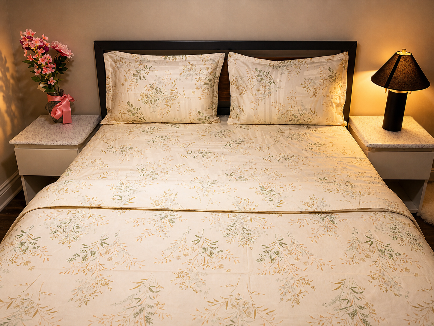 Bedroom with a bed featuring floral bedding, two nightstands with lamps, and a vase of flowers.
