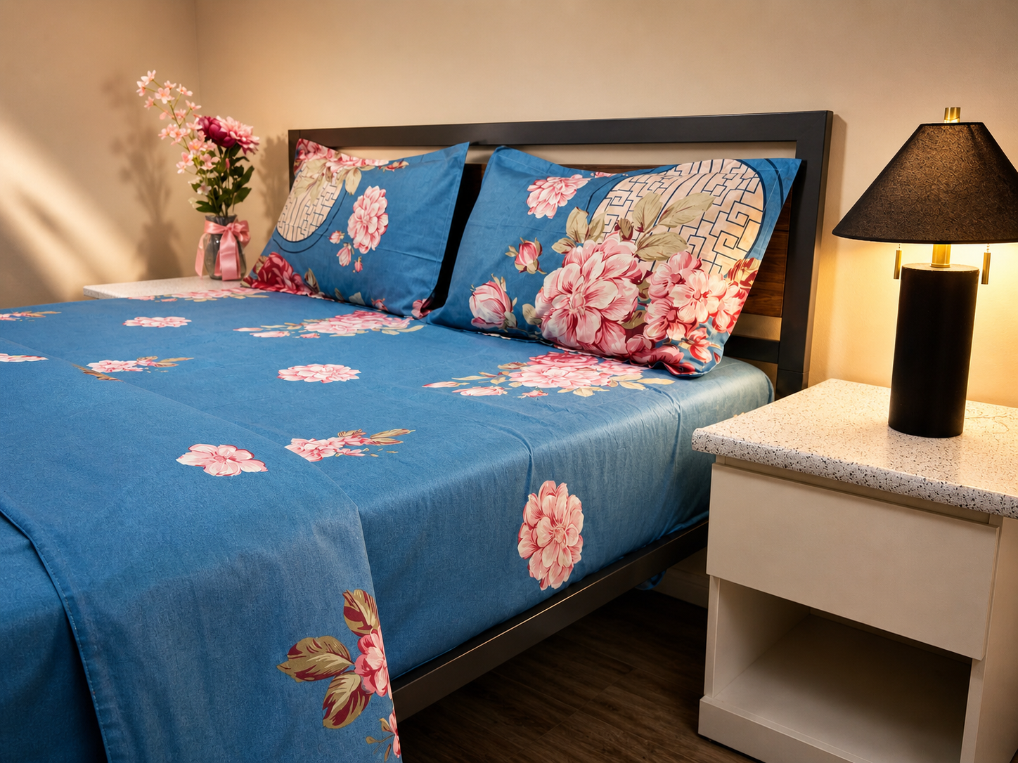 Bed with floral bedding and pillows next to a nightstand with a lamp.