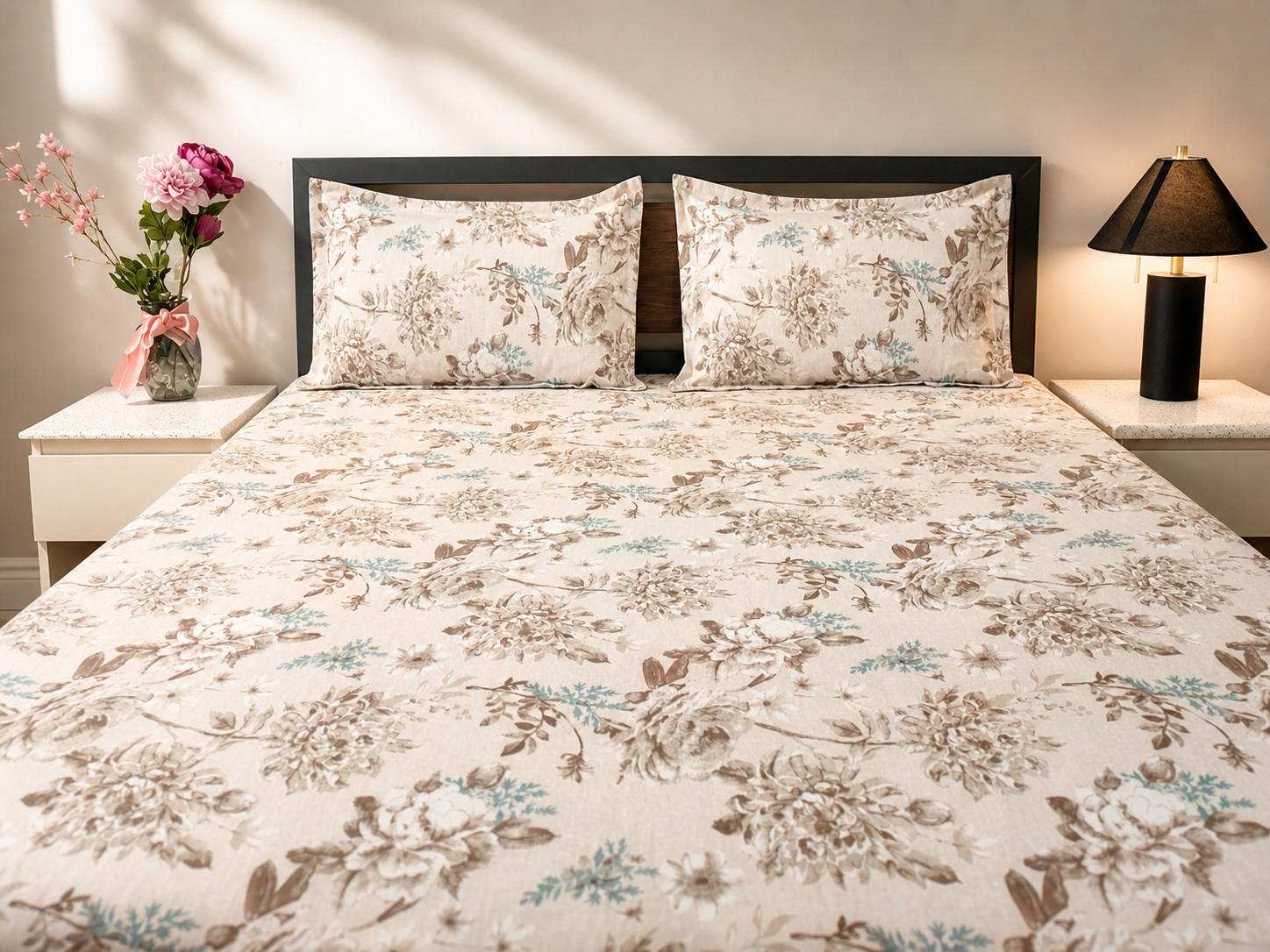 Floral patterned bedding set on a bed with matching pillows, nightstands, and a lamp.