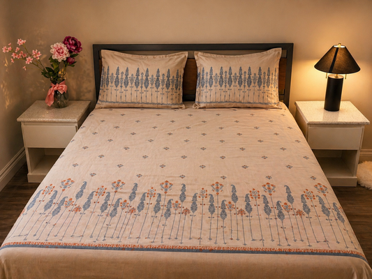 Bedroom with floral bedspread, pillows, and nightstands with lamp and flowers.